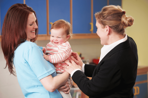 Mother handing baby over to nursery worker